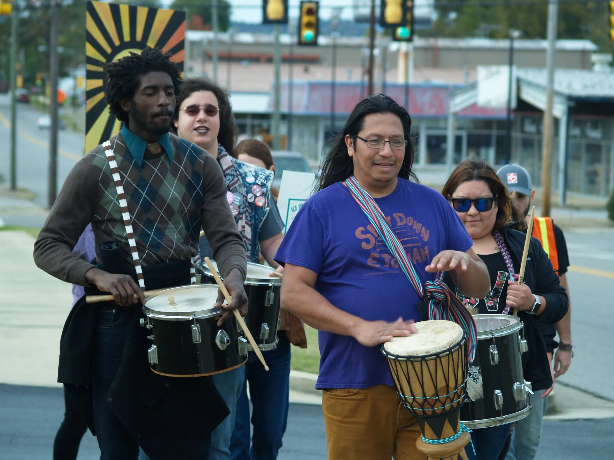 Group of people marching down the street with drums and signs protesting Etowah County Detention Center.