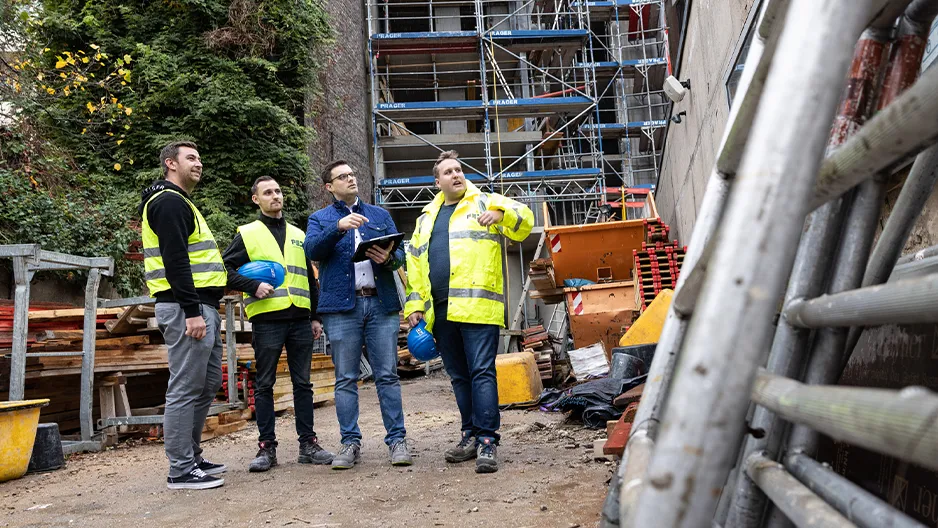 Baustelle heute – Ingenieure und Bauleiter mit Warnwesten im Gespräch vor Gebäude