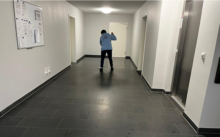Eine Person reinigt den Boden in einem weißen Flur mit dunklen Fliesen.
