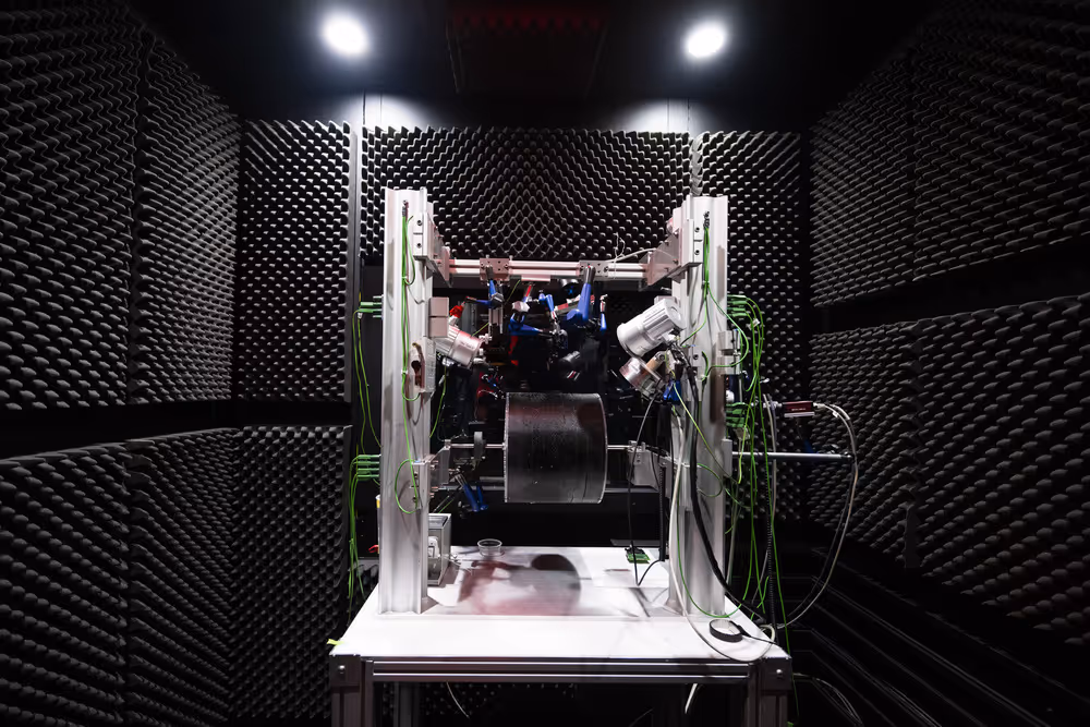 High-tech laboratory equipment with wires and sensors inside a soundproof room lined with black foam panels.