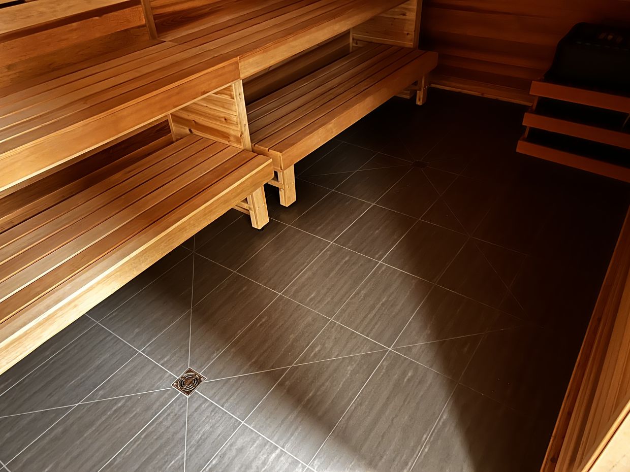 a cedar sauna with a dark large format floor with envelope cuts directing water to two separate drains. 