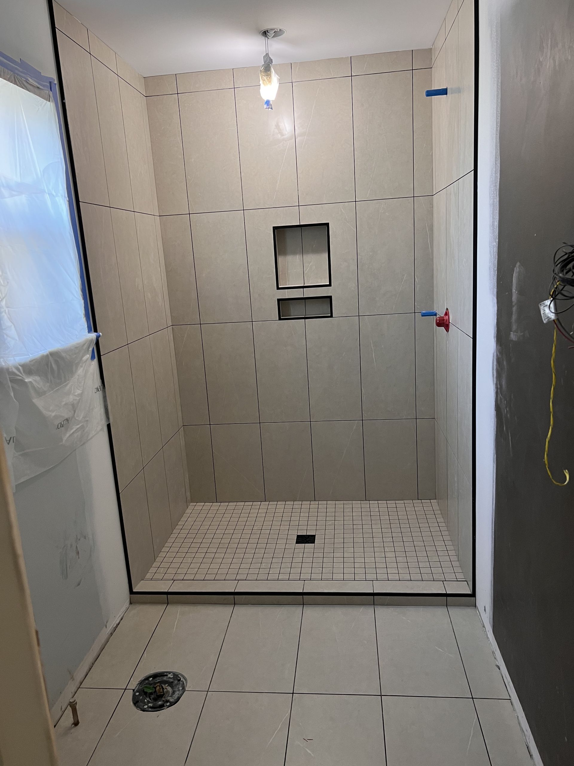 A walk in shower and bathroom floor installed with the same tile throughout. A light almond 12x24" tile.