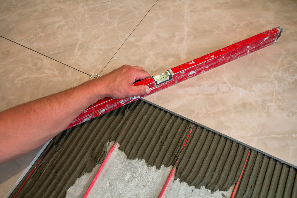 A man checking his tile work is flat and level using a level along the surface of the tile he is installing.