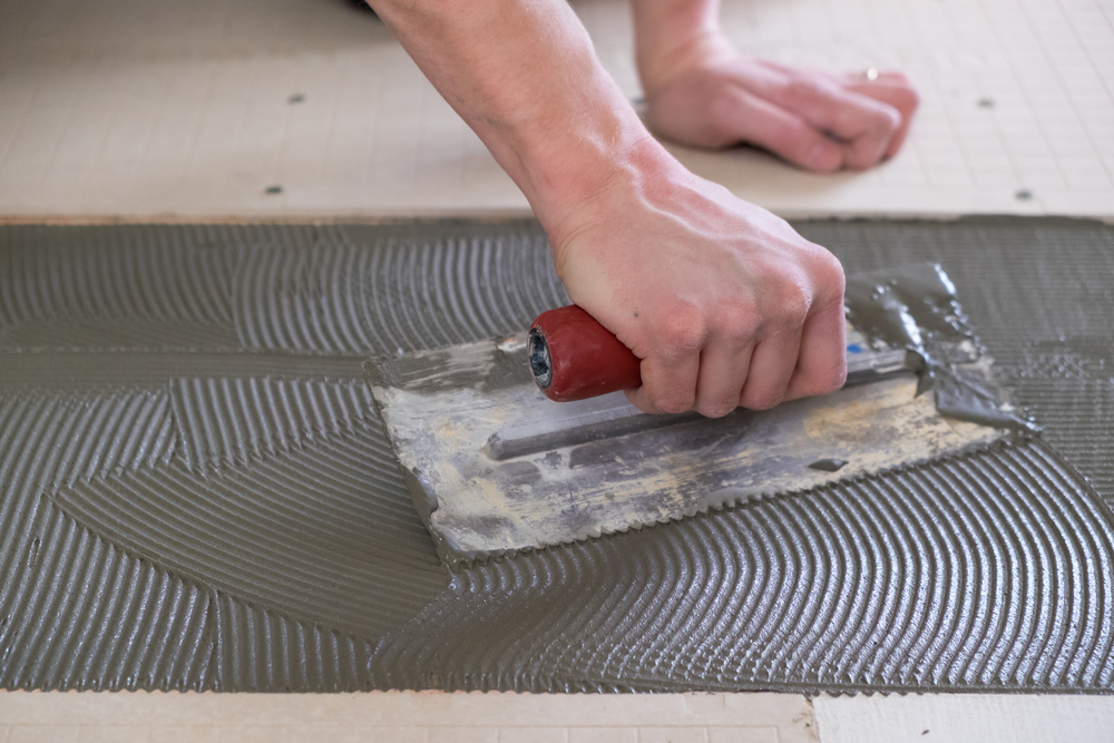 A man using a toothed trowel to spread thinset