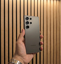 Hand holding a Samsung smartphone with multiple cameras on the back against a vertical wooden panel background.