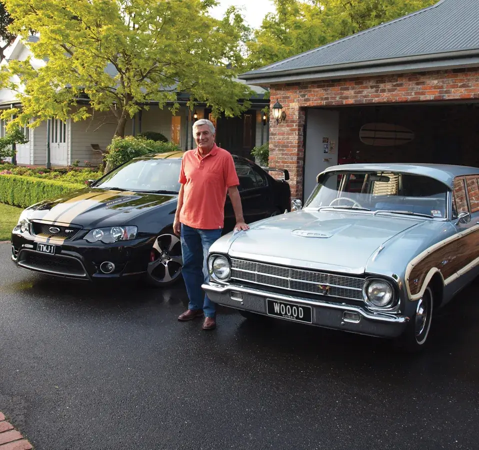 Classic car owner standing proudly in driveway with his black Ford GT and silver Ford Falcon wagon, featured in Shannons Insurance for Motoring Enthusiasts TV commercial.