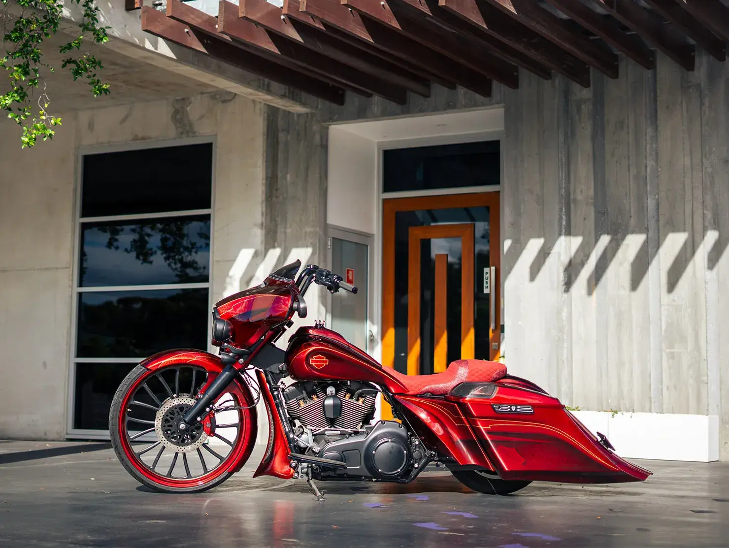Red custom Harley-Davidson bagger motorcycle with oversized front wheel, photographed in modern urban setting - Shannons Vehicle Photography