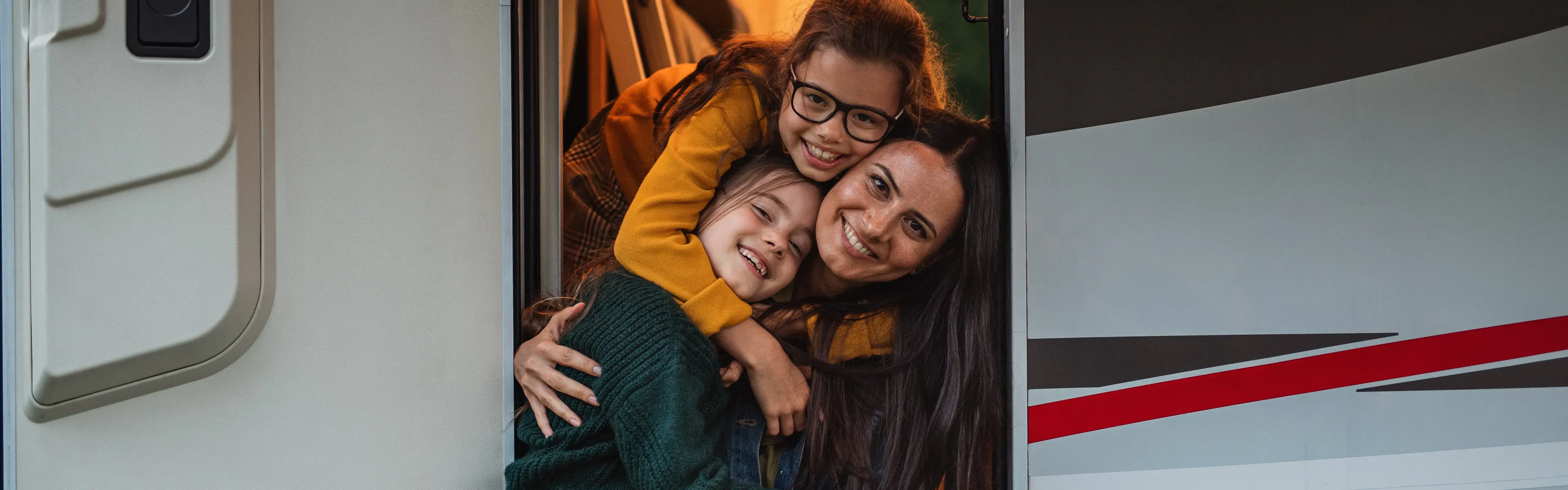 Mother and two daughters smiling and hugging in the doorway of a caravan during a holiday escape, part of the CIL Weekends campaign celebrating memorable getaways.