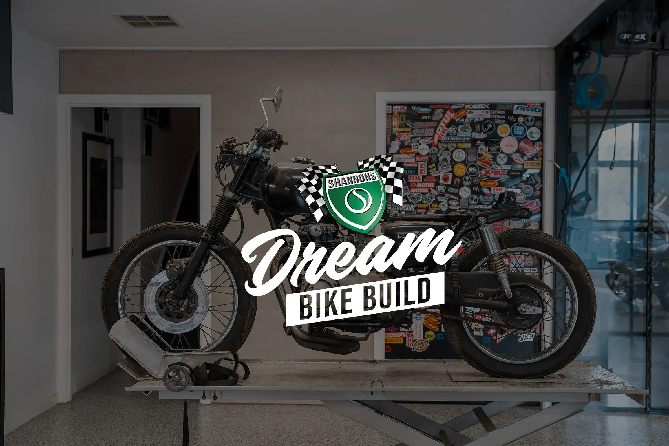 A vintage motorcycle sits on a workshop bench at the start of its restoration, overlaid with the Shannons Dream Bike Build logo, marking the launch of the Shannons Dream Bike Build YouTube Series.