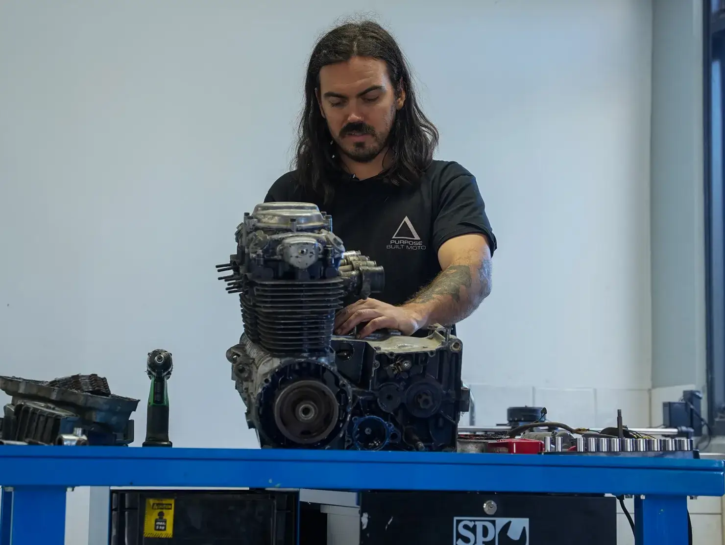 A builder inspects and works on the disassembled motorcycle engine at his bench, a pivotal step in the Shannons Dream Bike Build YouTube Series.