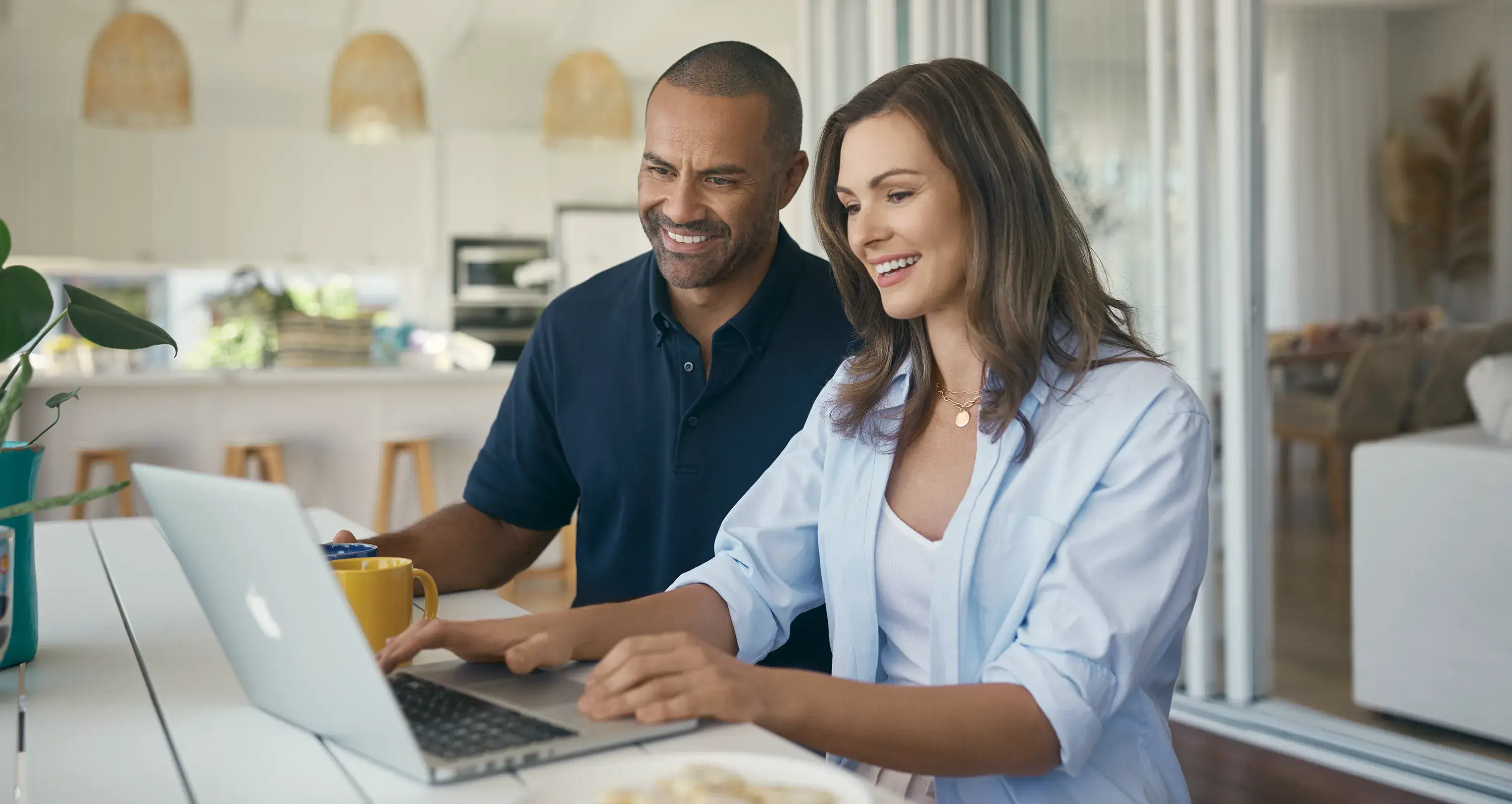 Couple smiling while using a laptop at a holiday rental property, hero image for Terri Scheer Holiday Rental Insurance campaign.