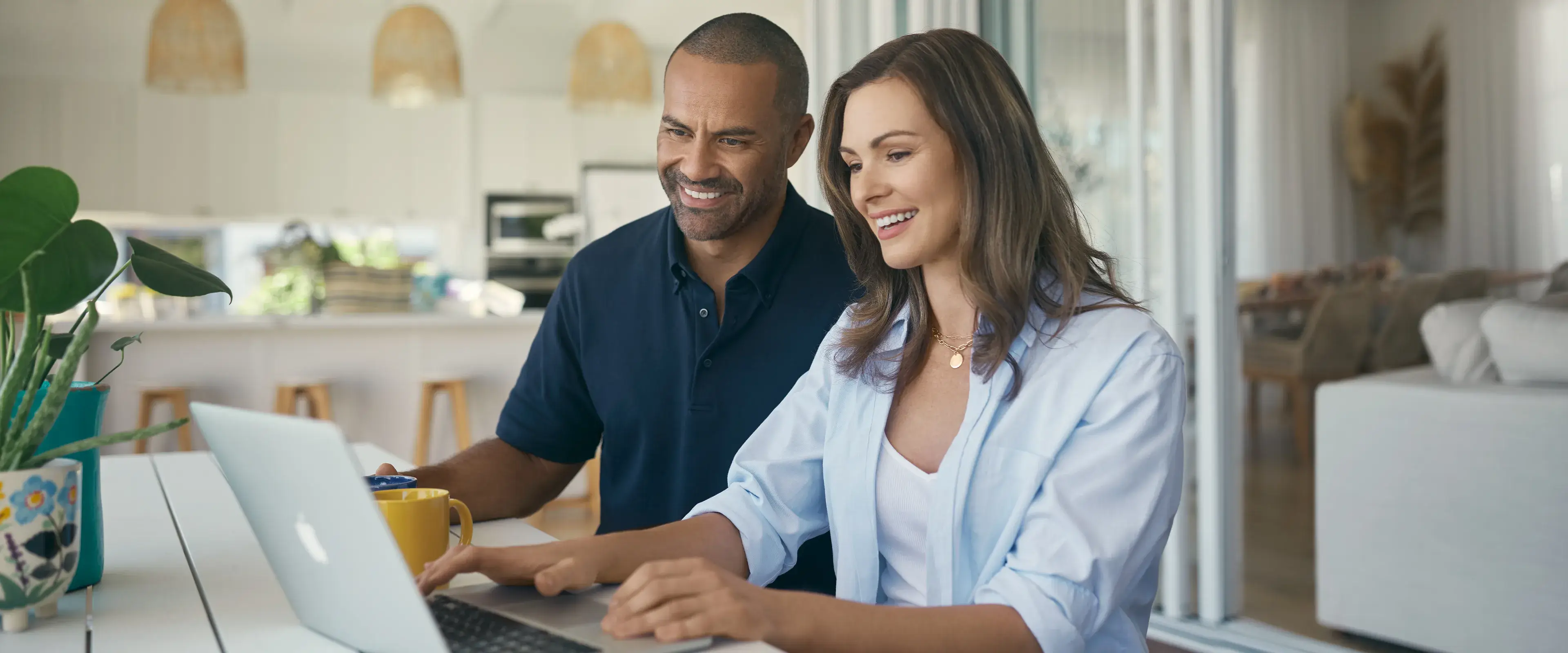 Couple smiling while using a laptop at a holiday rental property, hero image for Terri Scheer Holiday Rental Insurance campaign.