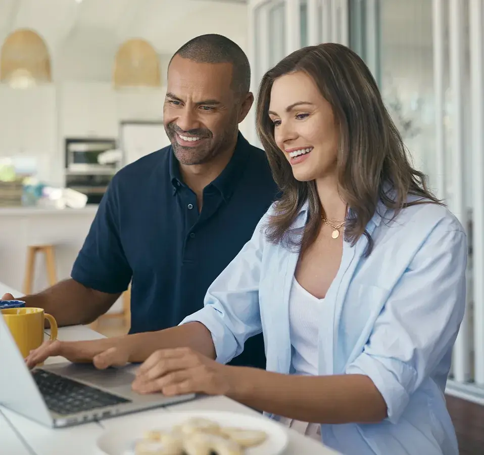 Couple smiling while using a laptop at a holiday rental property, hero image for Terri Scheer Holiday Rental Insurance campaign.