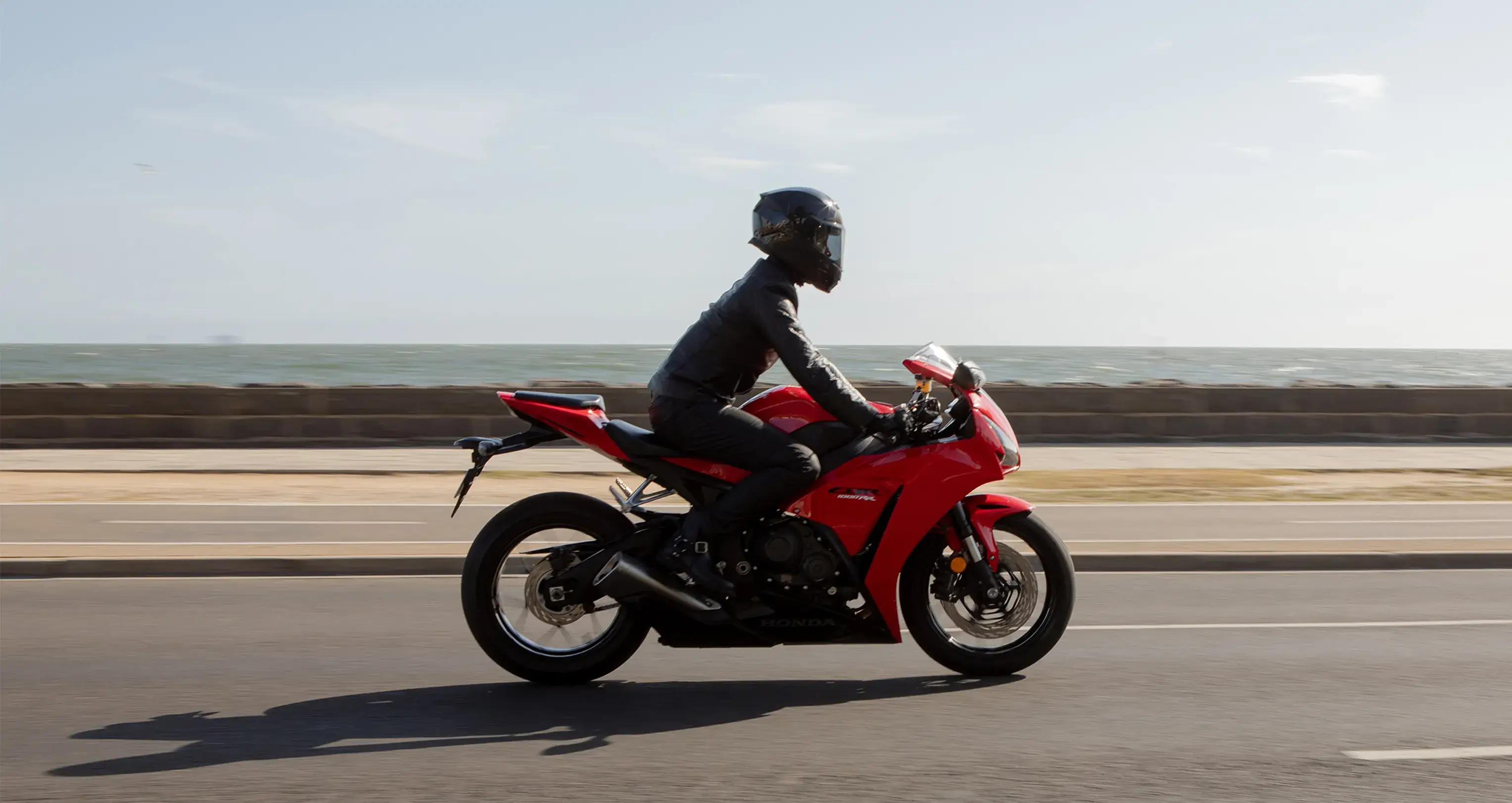Rider on a Honda sports motorcycle cruising along a coastal road with the ocean in the background, featured as part of the Shannons Bike Insurance campaign.