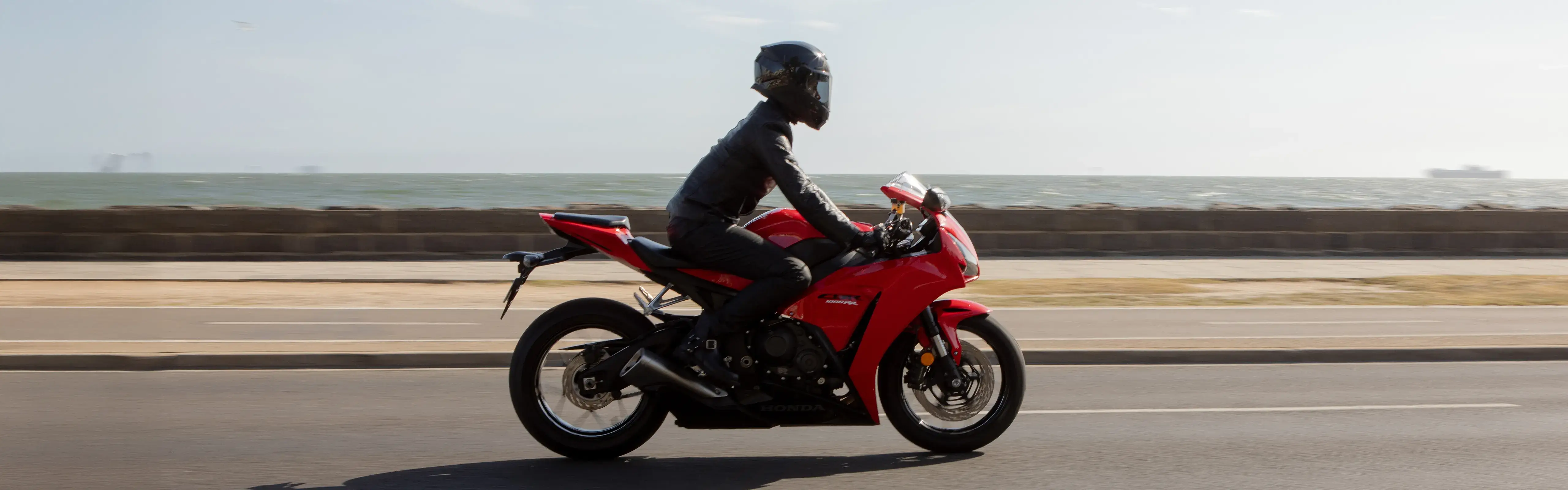 Rider on a Honda sports motorcycle cruising along a coastal road with the ocean in the background, featured as part of the Shannons Bike Insurance campaign.