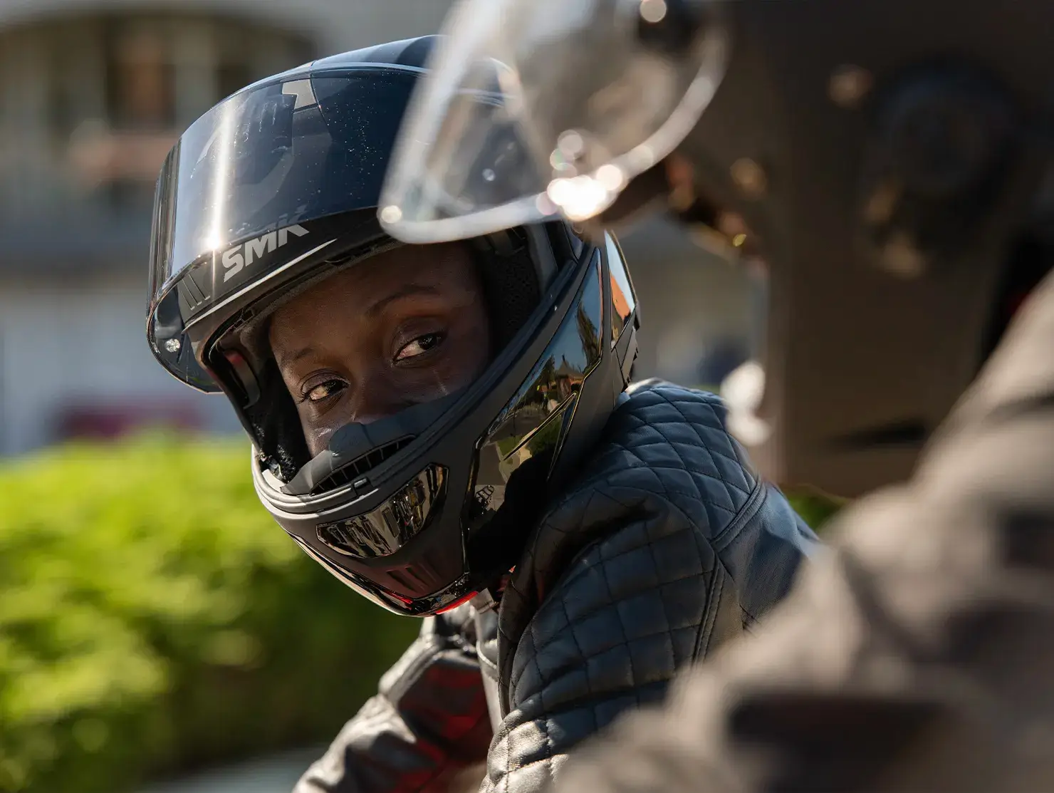Two riders in conversation, one looking across through a helmet visor, featured in the Shannons Bike Insurance campaign.
