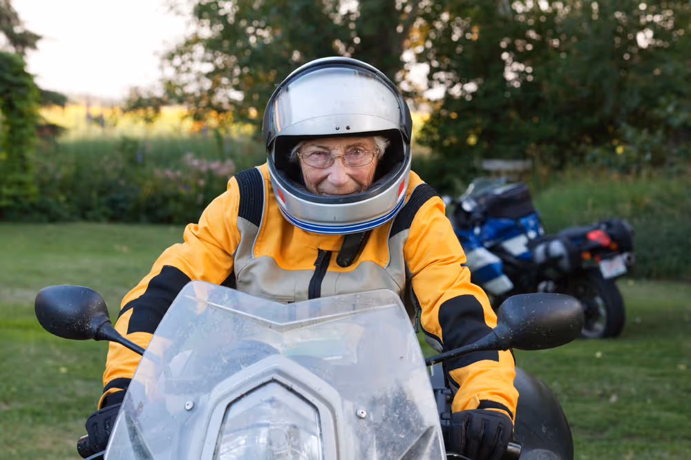 An older women driving a motorcycle with a helmet on