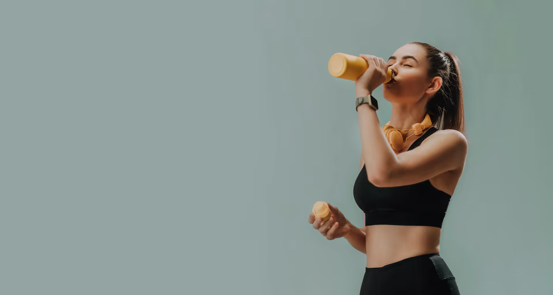 Woman in sportswear drinking from a yellow bottle.