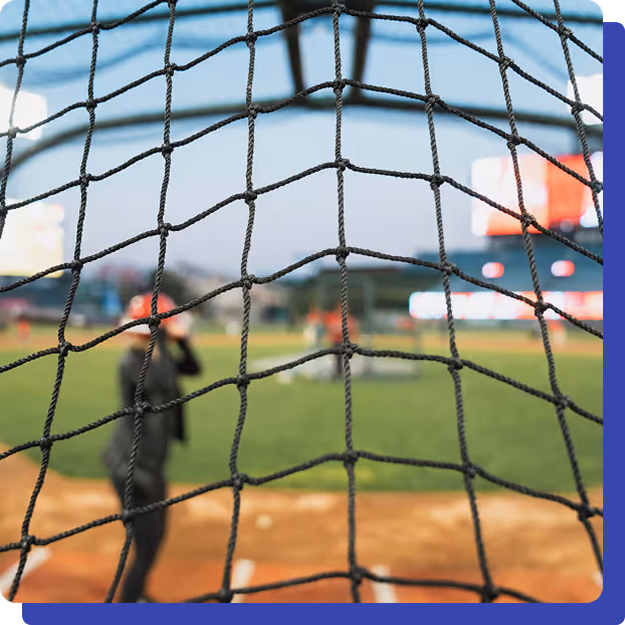 Close-up of a safety net at a baseball field with blurred players and stadium lights in the background.