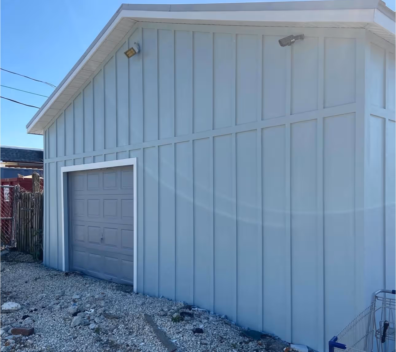 Light blue garage door on a light blue paneled building with gravel ground and a shopping cart on the right side.