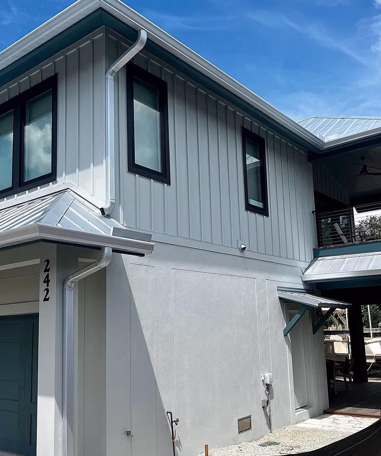 Modern two-story house exterior with gray panel siding, black-framed windows, and metal roofs under clear blue sky.
