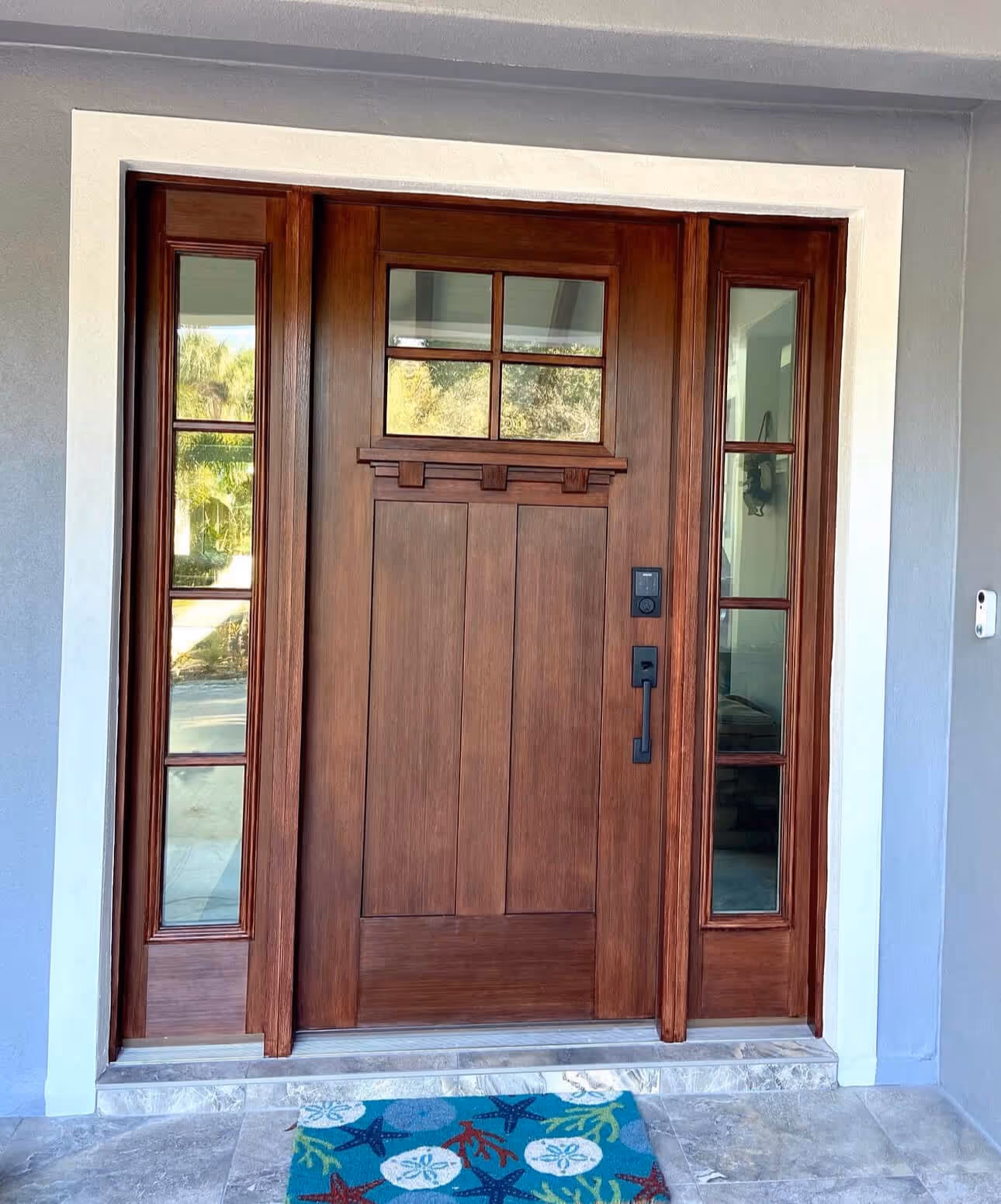 Wooden front door with four glass panes at the top and vertical sidelights on each side, with a blue sea-themed doormat in front.