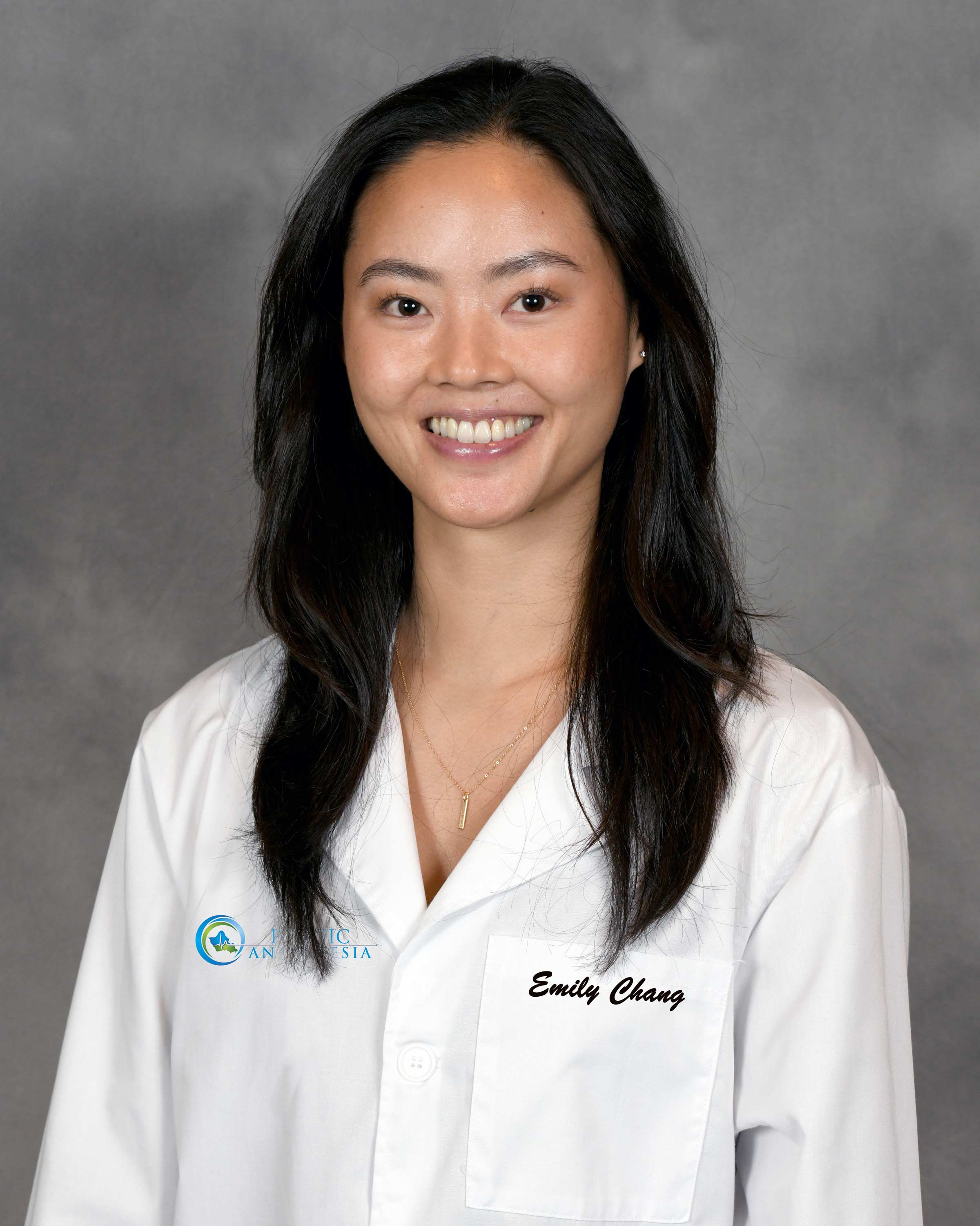 Smiling woman with long dark hair wearing a white lab coat with the name Emily Chang embroidered on the pocket.