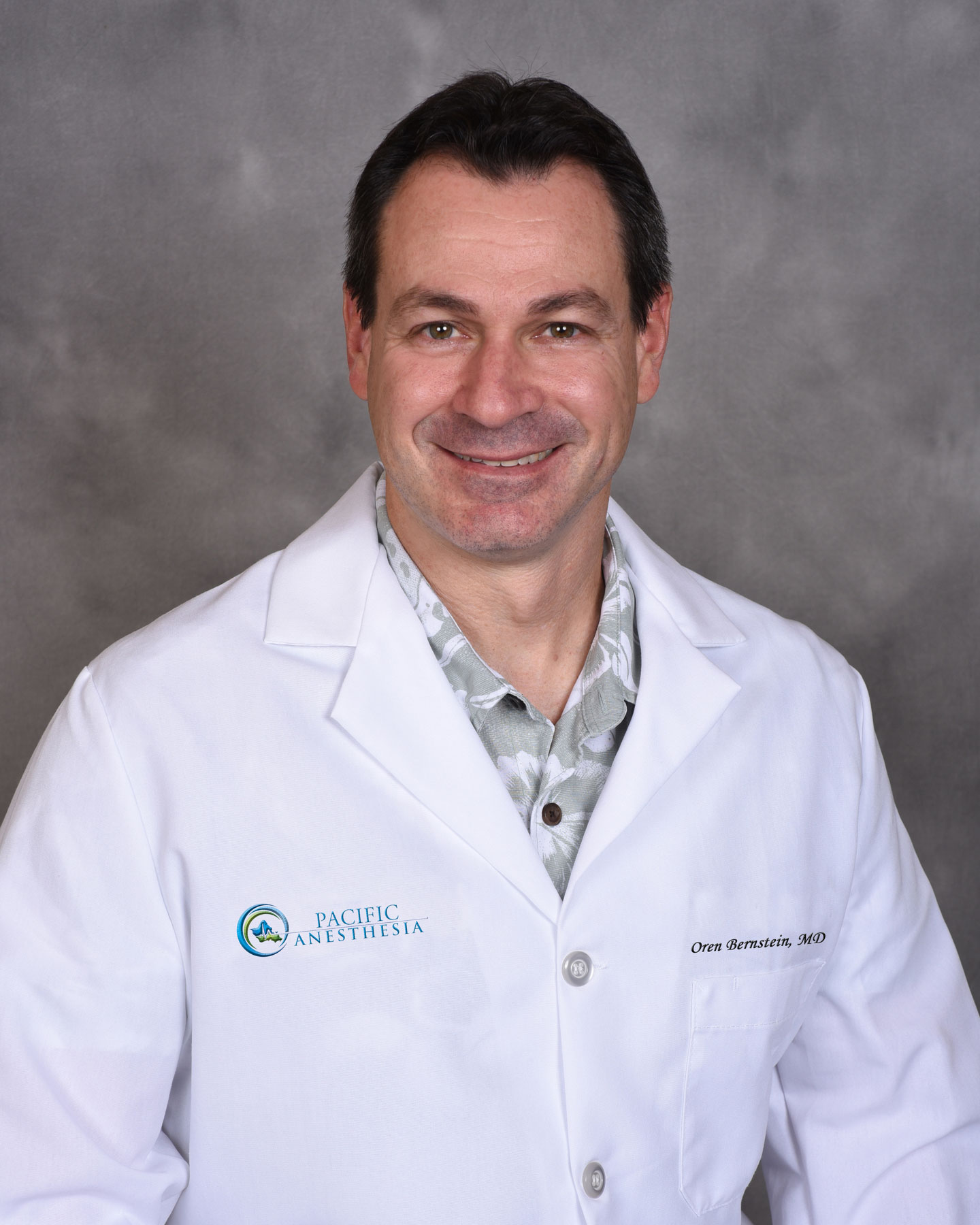 Smiling man wearing a white lab coat with Pacific Anesthesia logo and name tag reading Oren Bernstein, MD.