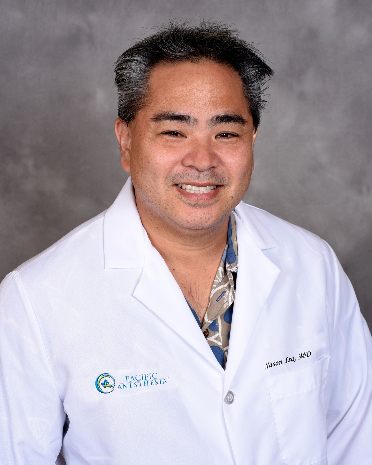 Smiling male doctor wearing a white coat with Pacific Anesthesia logo and name tag reading Jason Isa, MD.