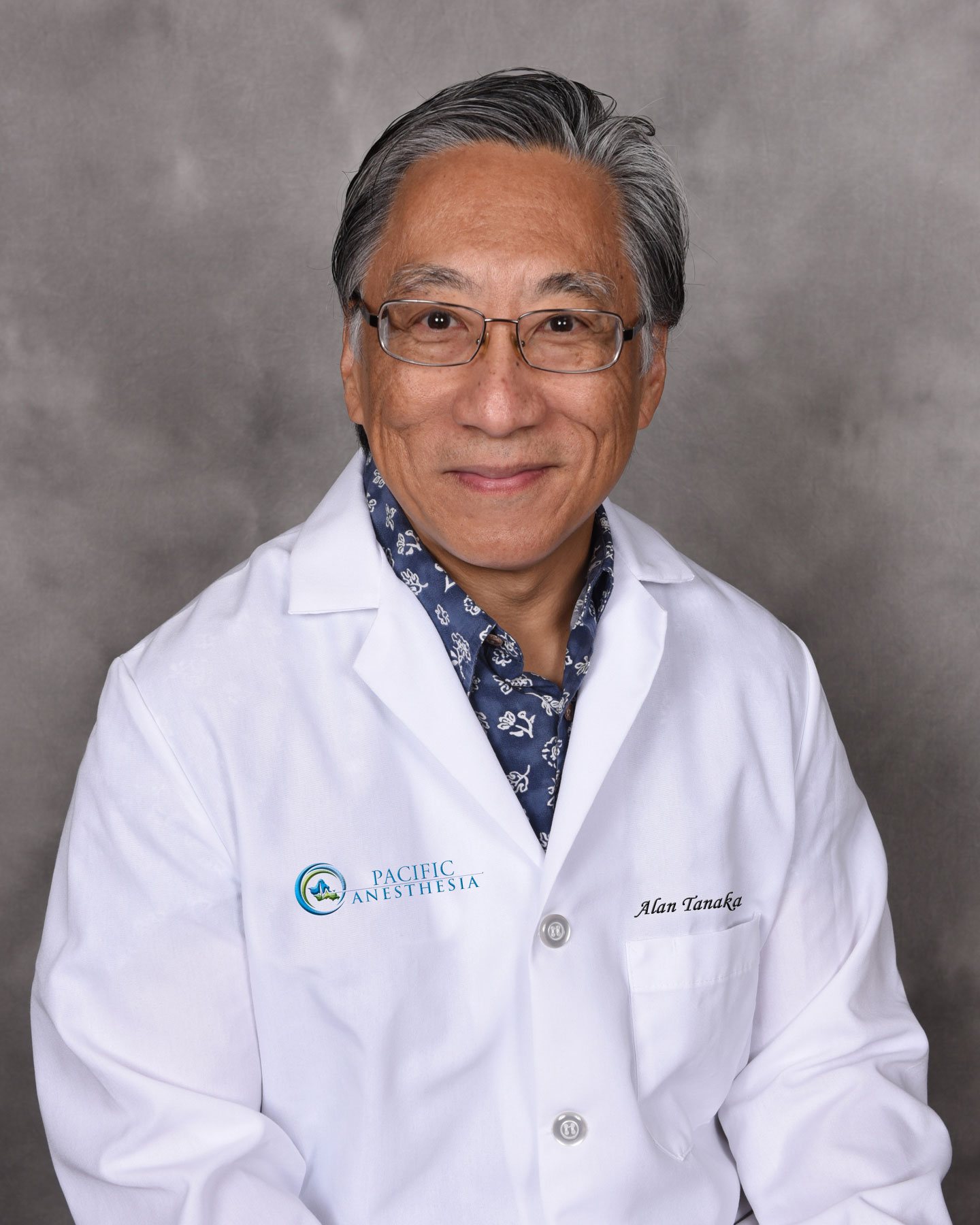Smiling man wearing glasses and a white lab coat with 'Pacific Anesthesia' logo and the name 'Alan Tanaka.'