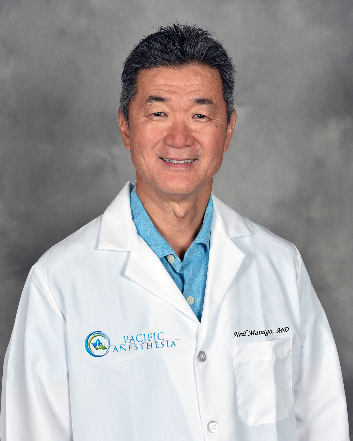 Smiling male doctor wearing a white lab coat with Pacific Anesthesia logo and name Neil Manago, MD.