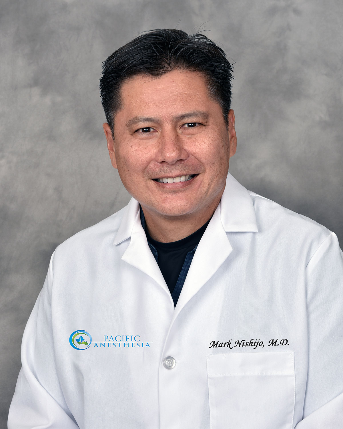 Smiling male doctor in a white coat with Pacific Anesthesia logo and name Mark Nishijo, M.D.