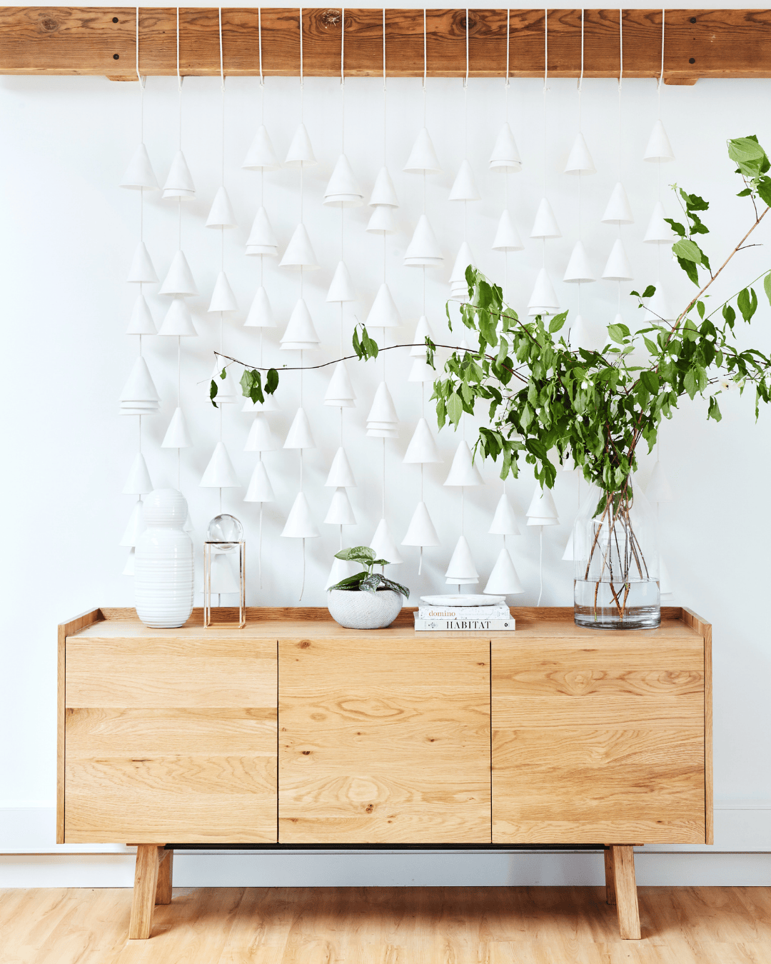 Three women collaborating over a paper with a ruler, one holding a ceramic mug, at a desk with pencils and a sharpener.