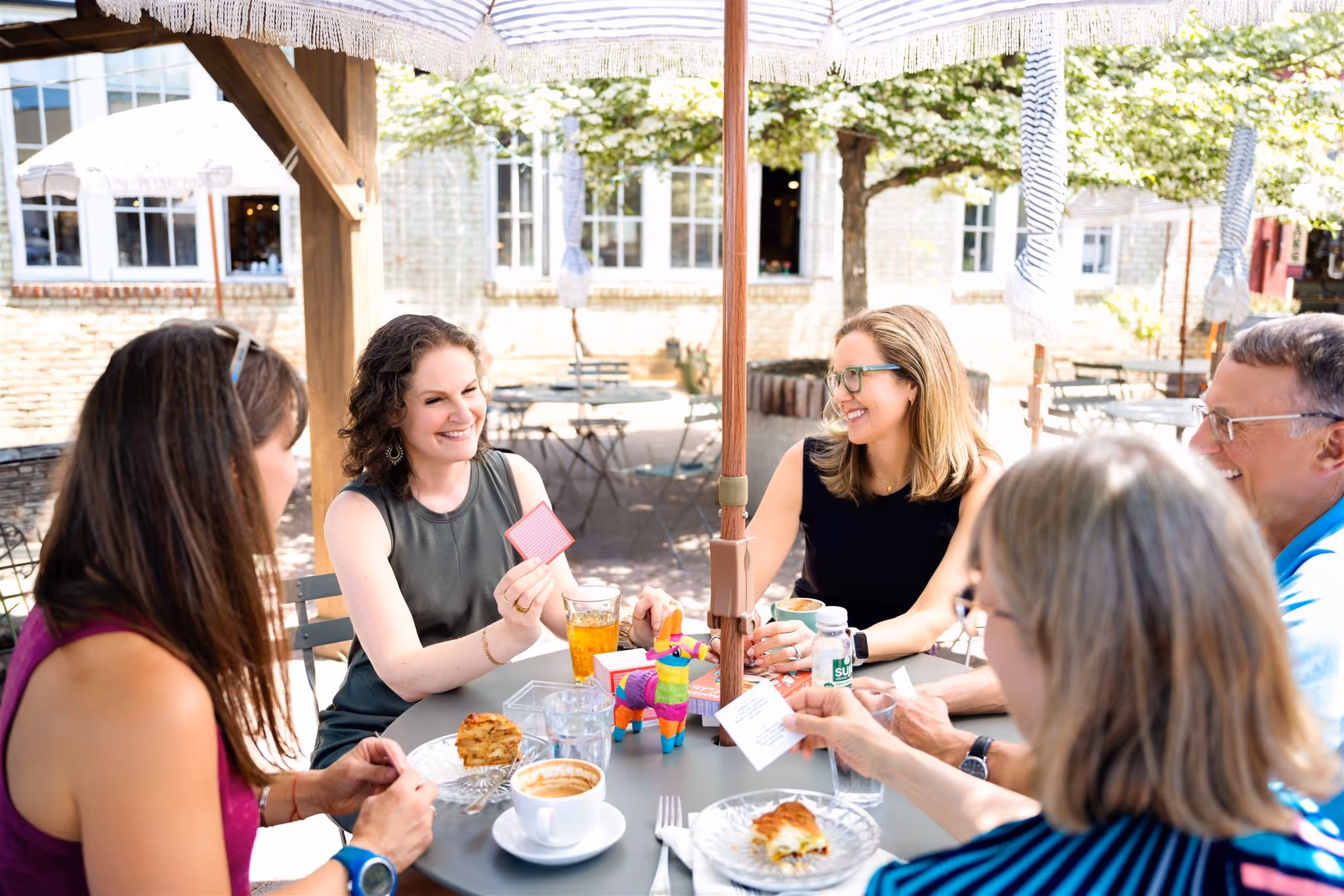 Adults playing Spanish language games around an outdoor table with Gringo Language Academy in Bend, Oregon, with a piñata, food, and drinks.