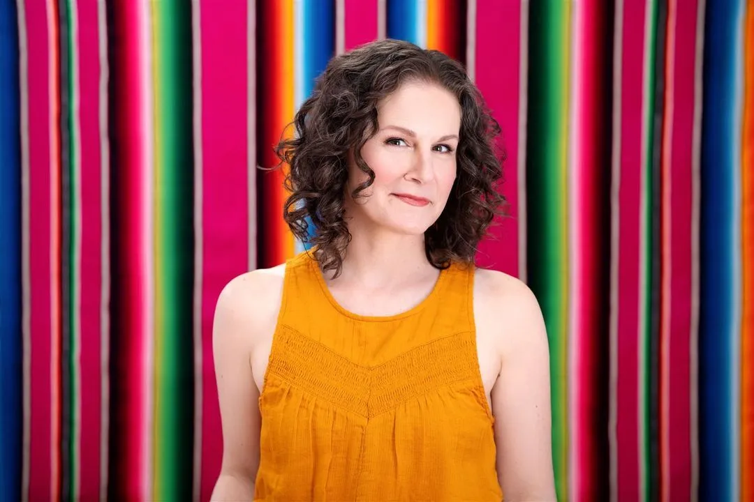 Jennifer Colestock, Chief Spanish Officer at Gringo Language Academy in Bend, Oregon, standing before a vibrant Mexican sarape blanket.