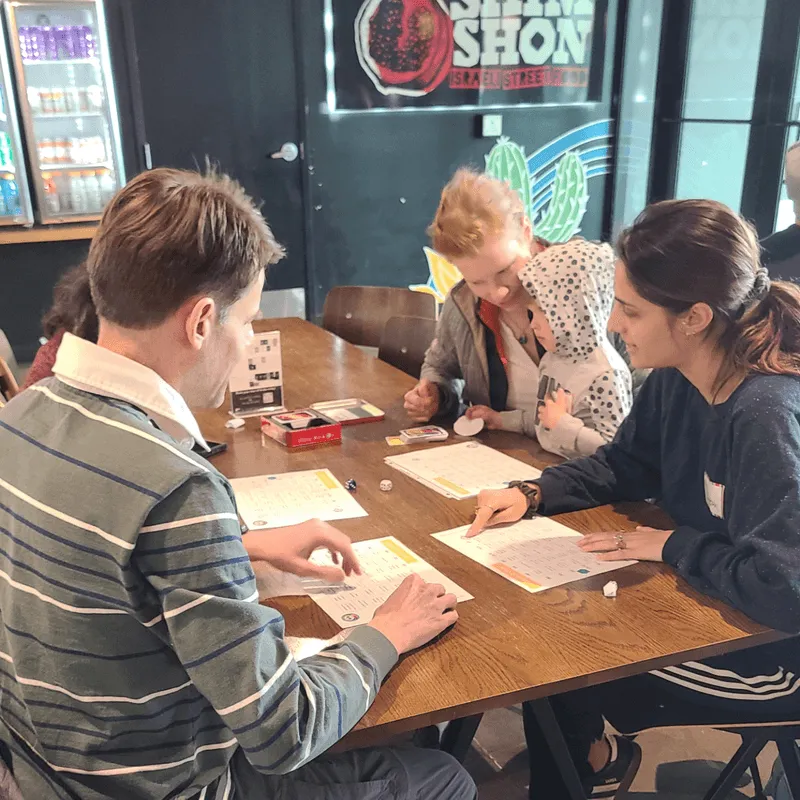 Adults and young children playing Spanish language games at the Lingo Latte Lounge MeetUp in Bend, Oregon—an in-person event hosted by Gringo Language Academy at The Grove Market Hall in Northwest Crossing.