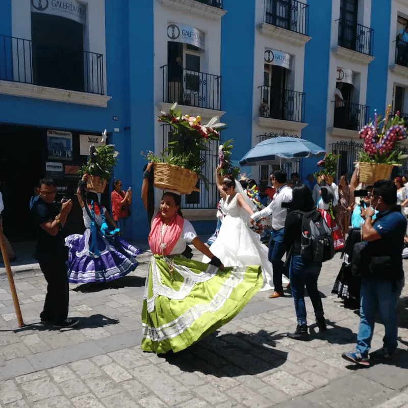 Colorful street parade in Oaxaca, Mexico with a woman in a lime green dress dancing in front of bright blue buildings—taken during a student trip