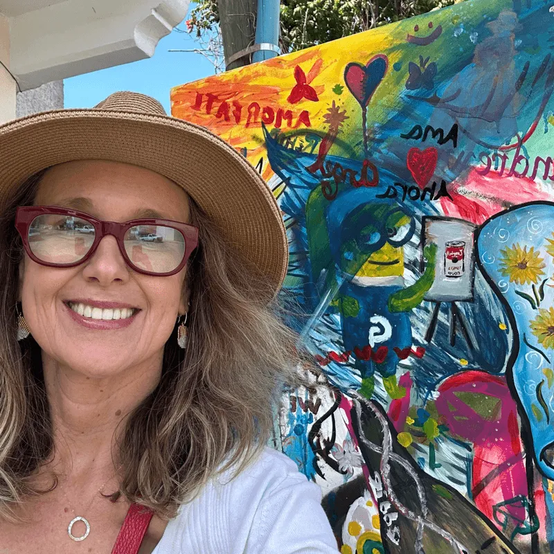 Katie R., from Bend, Oregon, beaming in front of a bright and colorful mural.