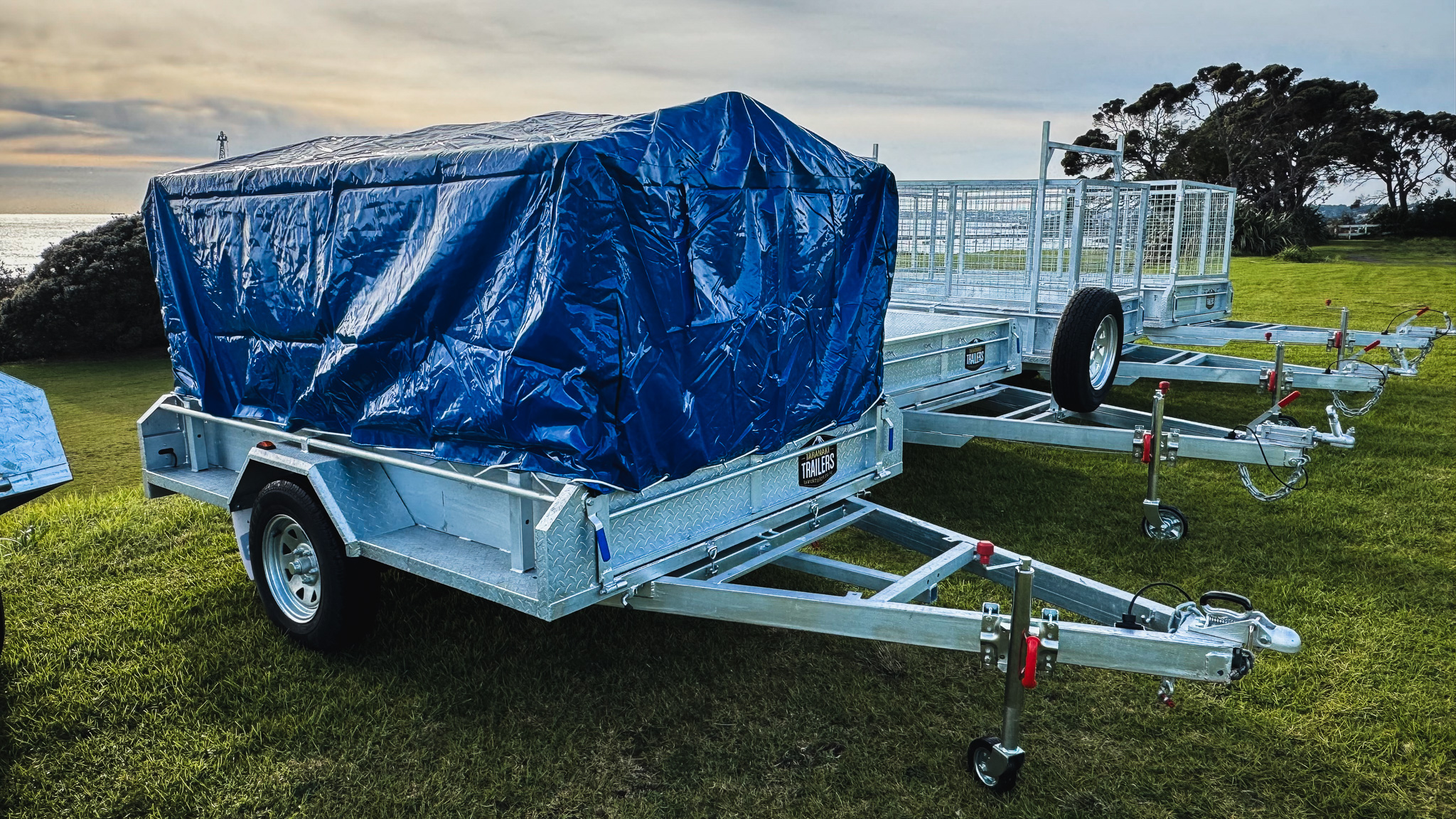 Metal trailers parked on grass with one covered by a blue tarp