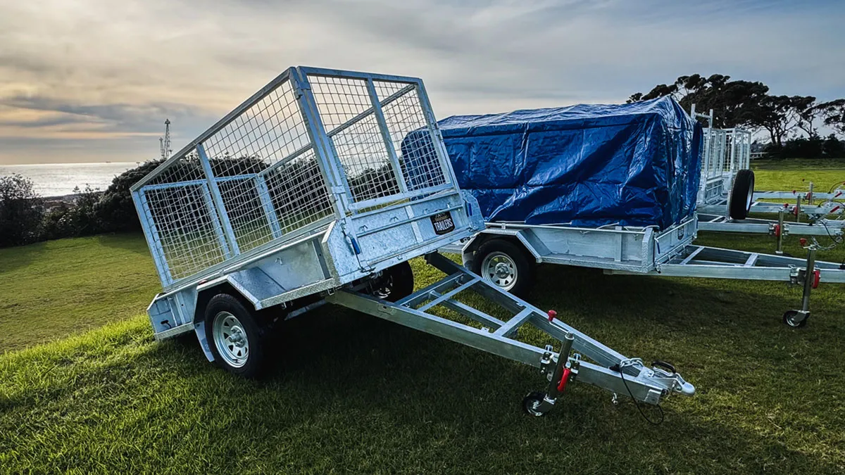 Single-axle metal utility trailer with cage sides parked on grass.