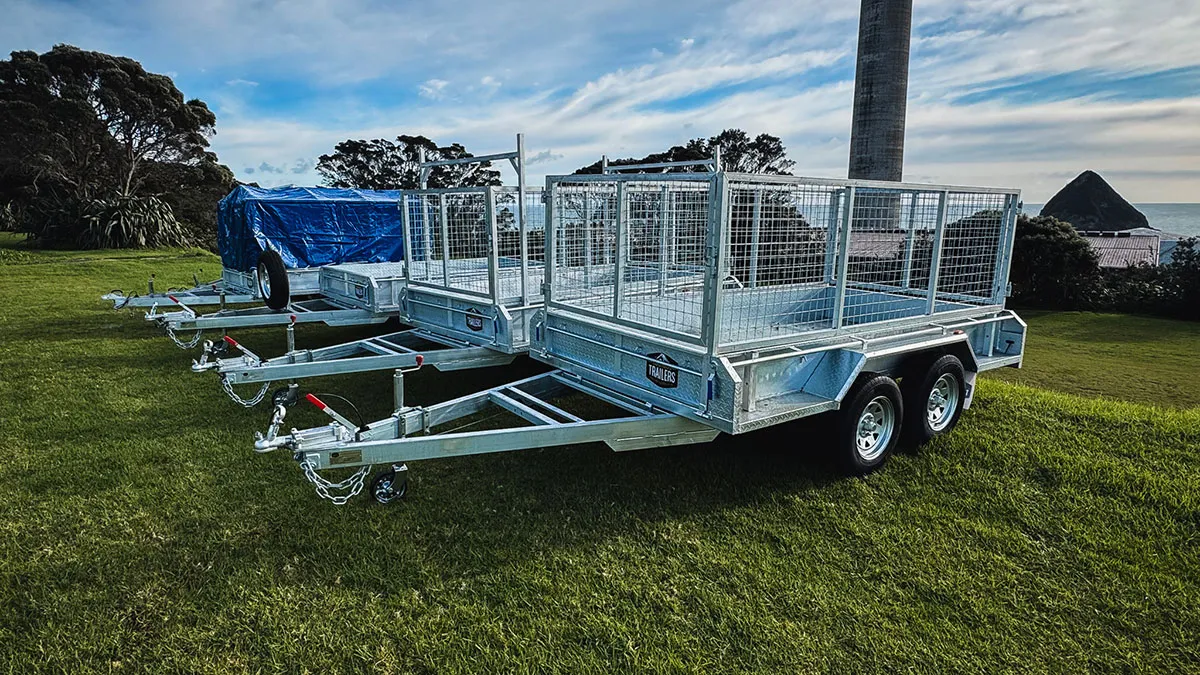 Three metal utility trailers lined up on grass with a blue tarp on the furthest trailer.