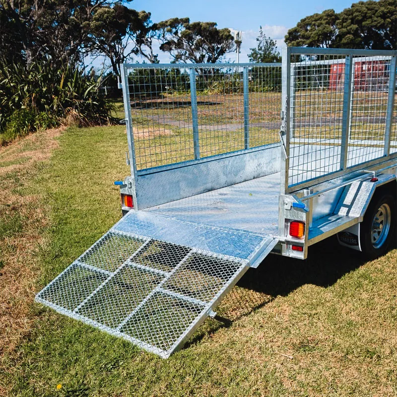 Silver metal trailer with mesh sides and ramp gate open on grassy ground.
