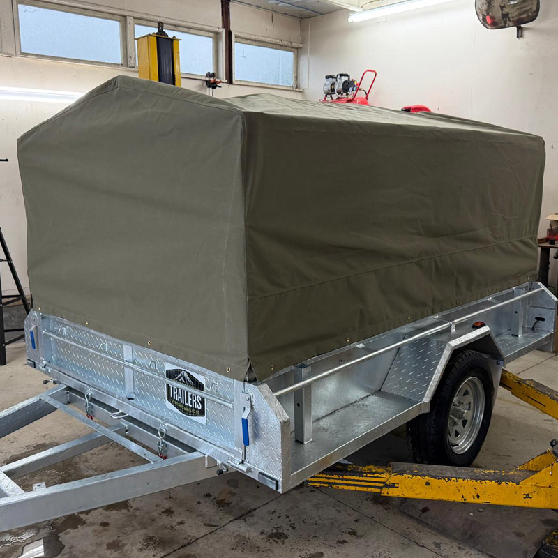 Metal trailer with olive green canvas cover parked inside a workshop.