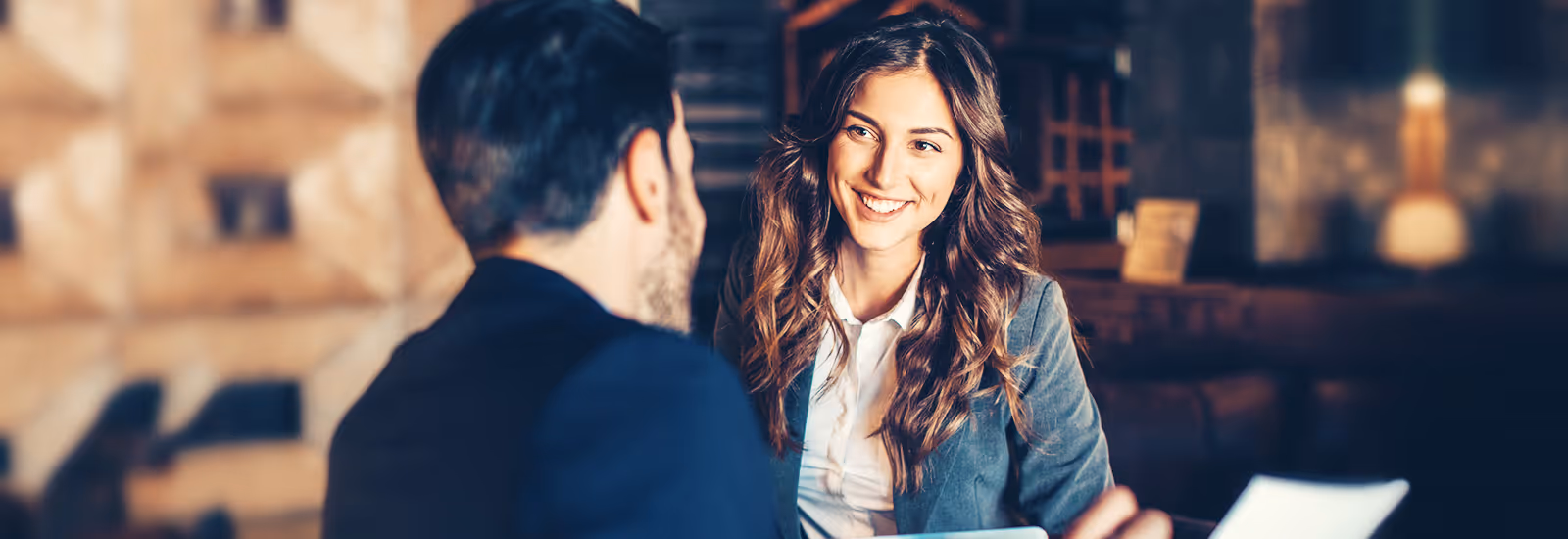 Smiling woman in business attire talking with a man in a cozy indoor setting.