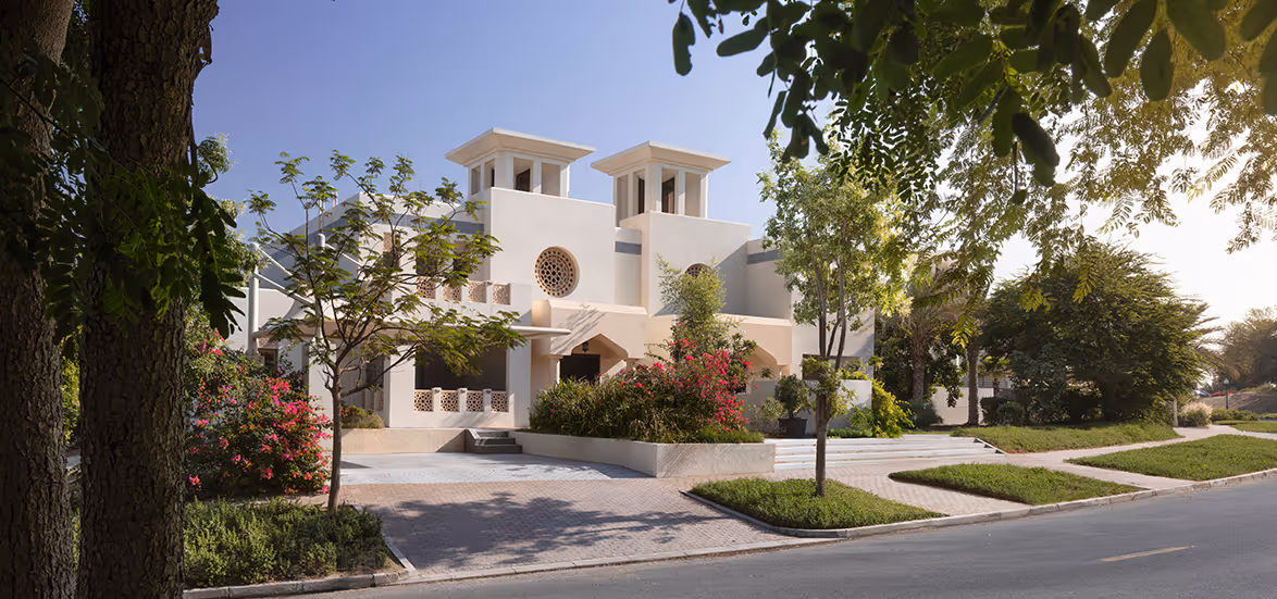 White modern villa surrounded by green trees and colorful flowering bushes under a clear blue sky.