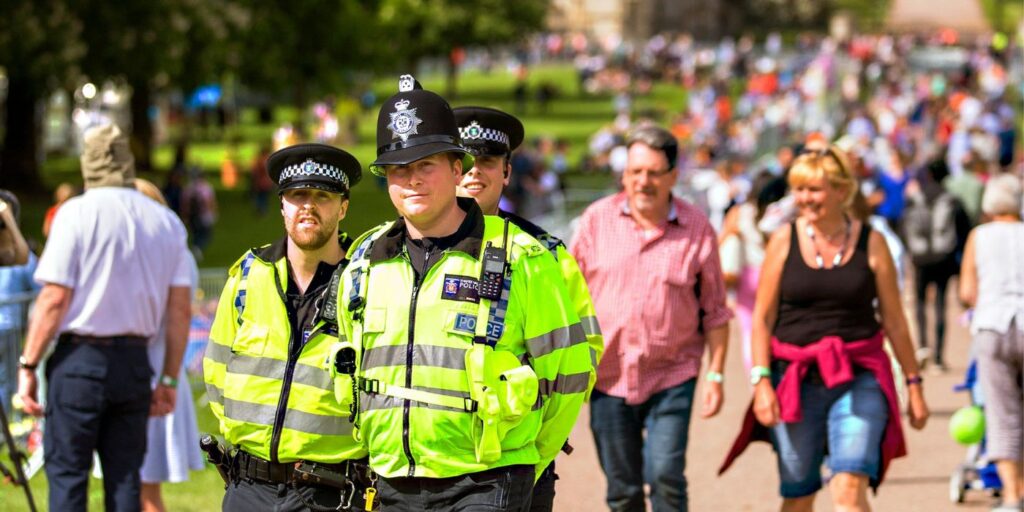 Police stare toward the camera smiling walking through a busy park