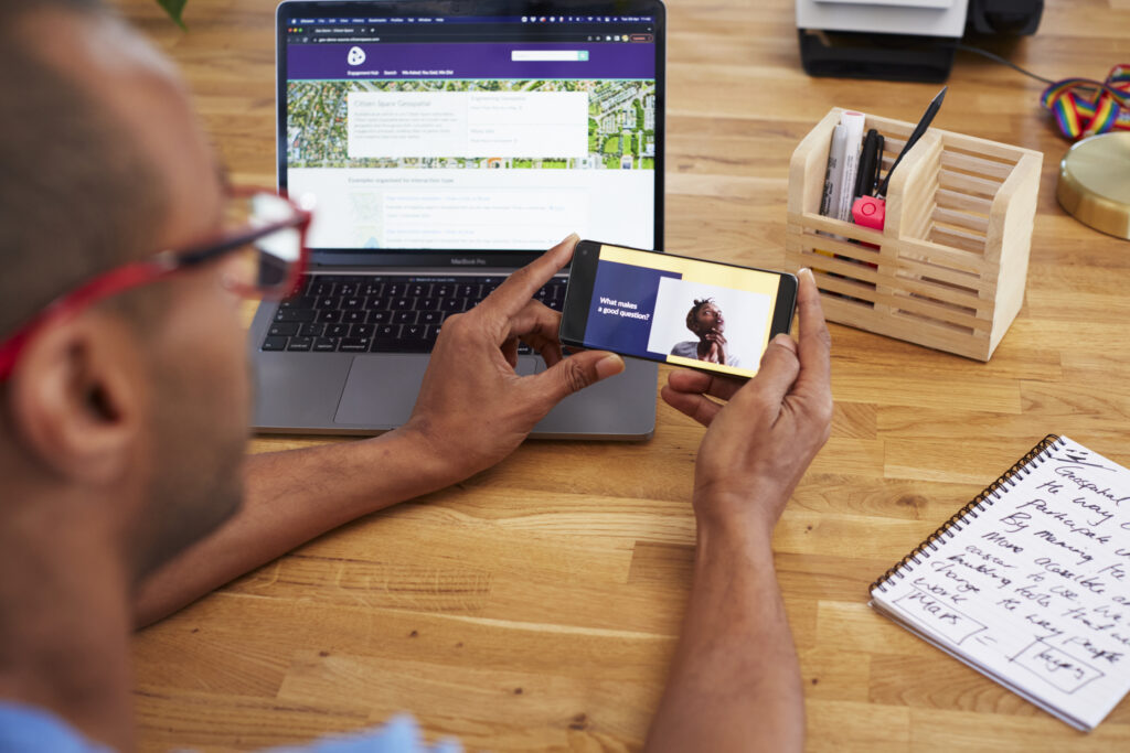 man sat at desk, computer in background opened to Citizen Space and he's holding a phone that asks 