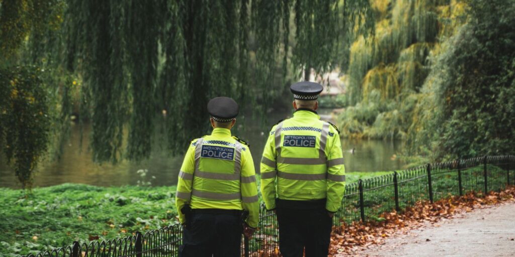 community policing - 2 police people facing away from the camera walking through a park