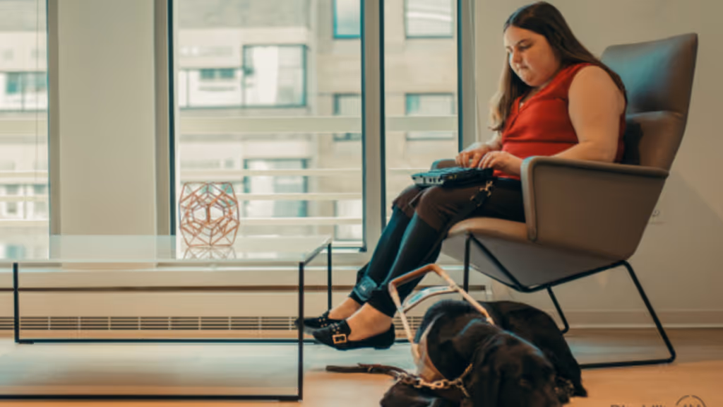a women with a disability and trained dog sat on chair with laptop on lap