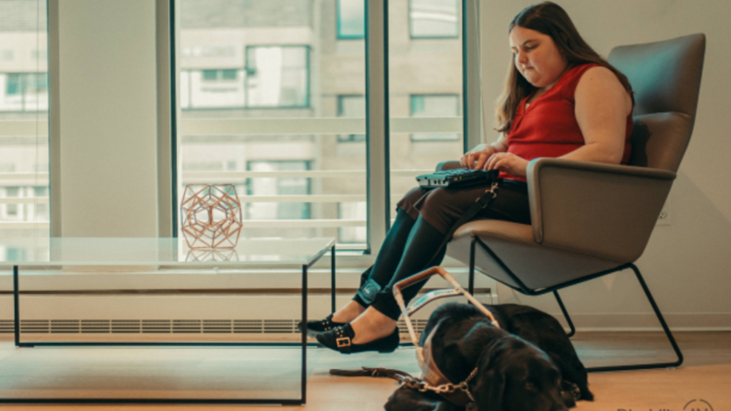 a women with a disability and trained dog sat on chair with laptop on lap 
